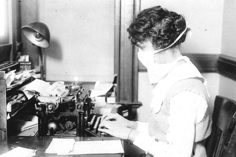 Mulher digitando na máquina de escrever usando uma máscara em 1918