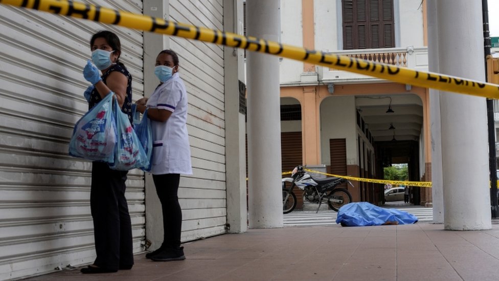 Duas mulheres em Guayaquil e ao fundo o corpo de um homem coberto na rua.