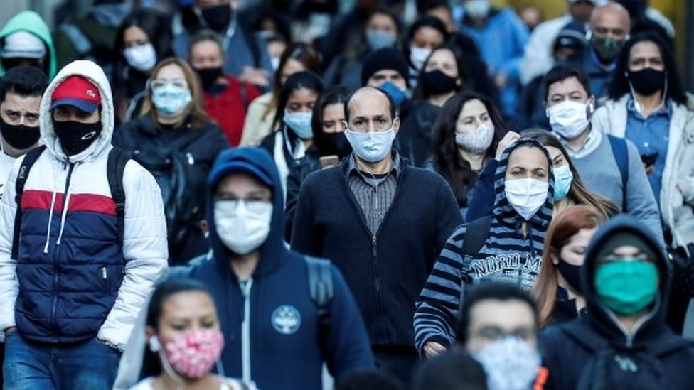 Pessoas andam na rua em São Paulo usando máscaras