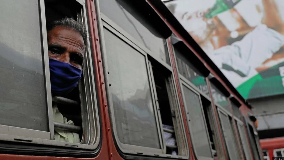 Homem de máscara com o rosto para fora da janela do ônibus olha para a câmera