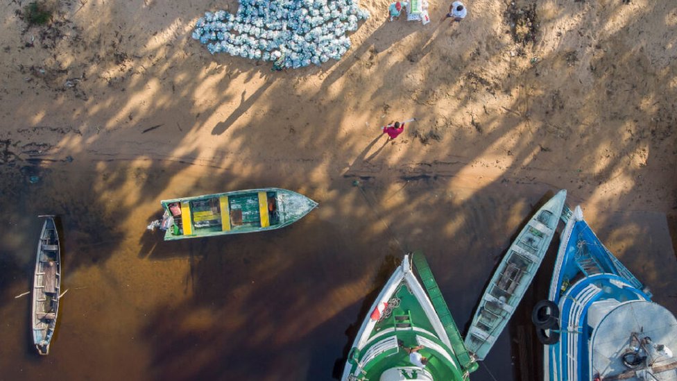 Vista aérea de kits de limpeza sendo entregues em comunidade à beira do rio