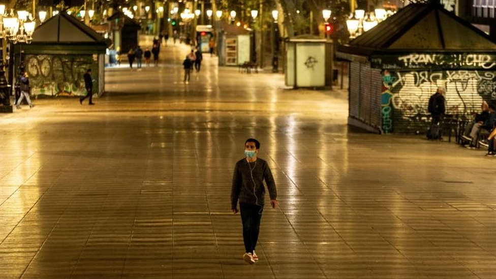 Homem de máscara caminha em rua de pedestres à noite