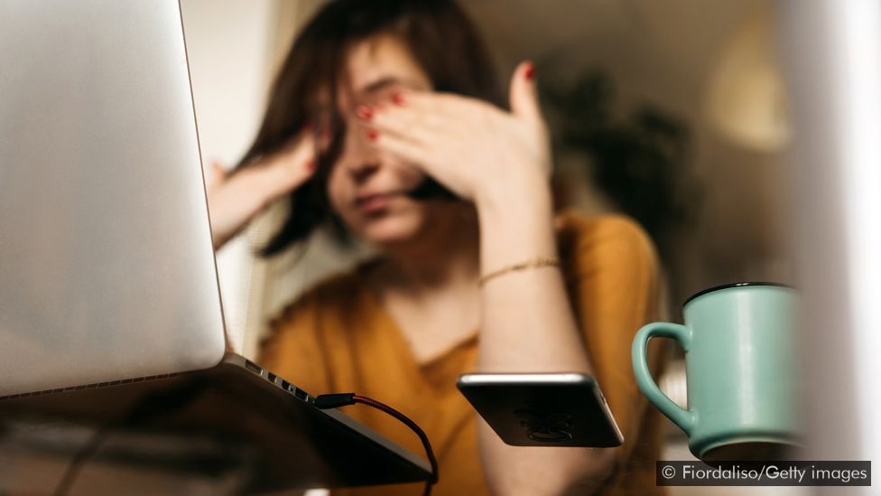 Mulher na frente do laptop tapando os olhos