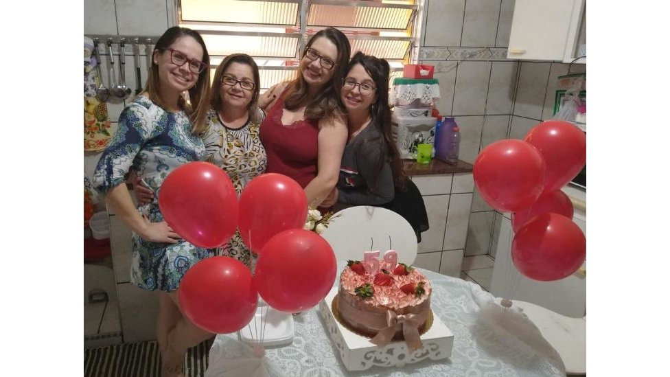 Ceci posa abraçada às três filhas em frente ao bolo de seu aniversário