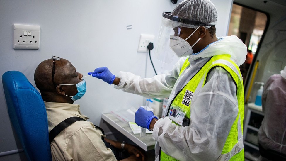 Um membro da equipe médica do Departamento de Saúde da África do Sul obtém uma amostra nasal de um passageiro em uma unidade móvel de teste no Aeroporto Internacional O.R. Tambo em Ekurhuleni em 30 de dezembro de 2020, onde os passageiros que apresentam sintomas de COVID-19 na chegada são testados