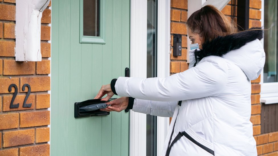 A voluntária Hanna Taylor entrega kits de teste de coronavírus de porta em porta em Woking, Surrey