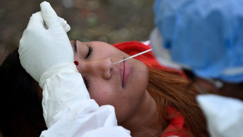 Profissional da saúde insere uma haste flexível no nariz de uma paciente para fazer um teste PCR numa paciente