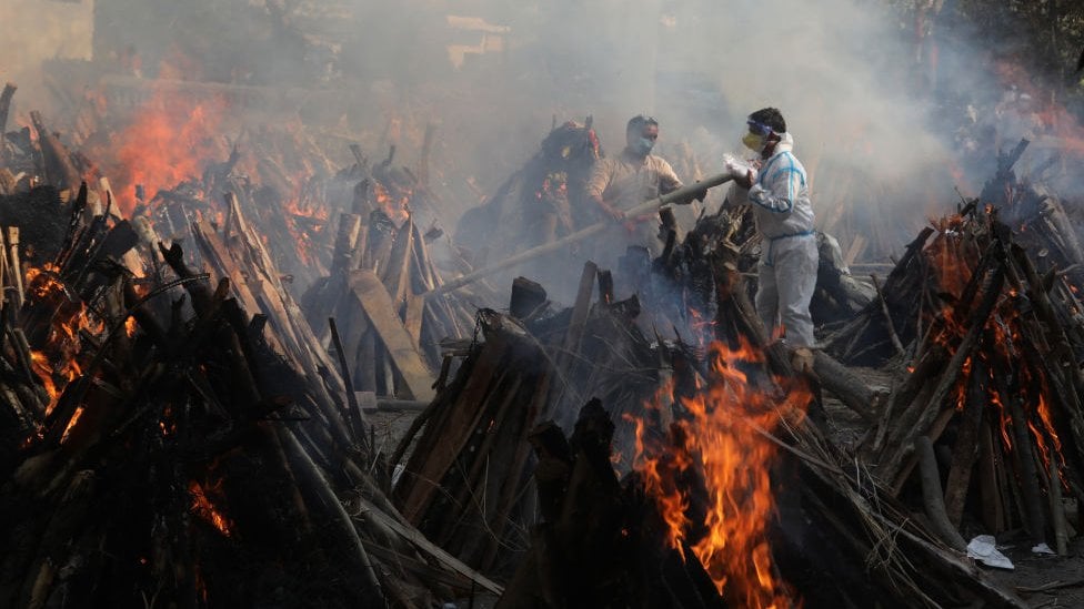 Parentes ao lado das piras funerárias daqueles que morreram devido à COVID-19, no crematório de Ghazipur, em Nova Delhi.