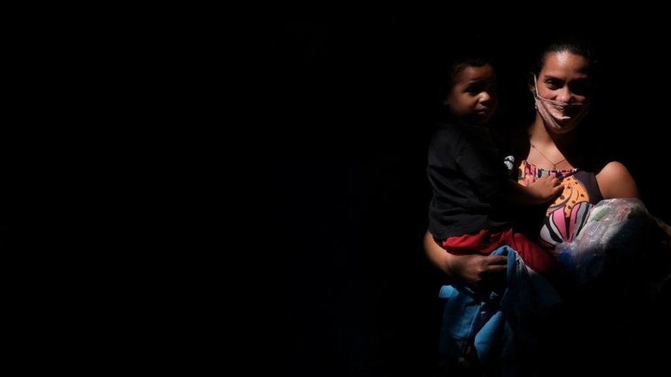 Mulher com pacote de comida e filho no colo