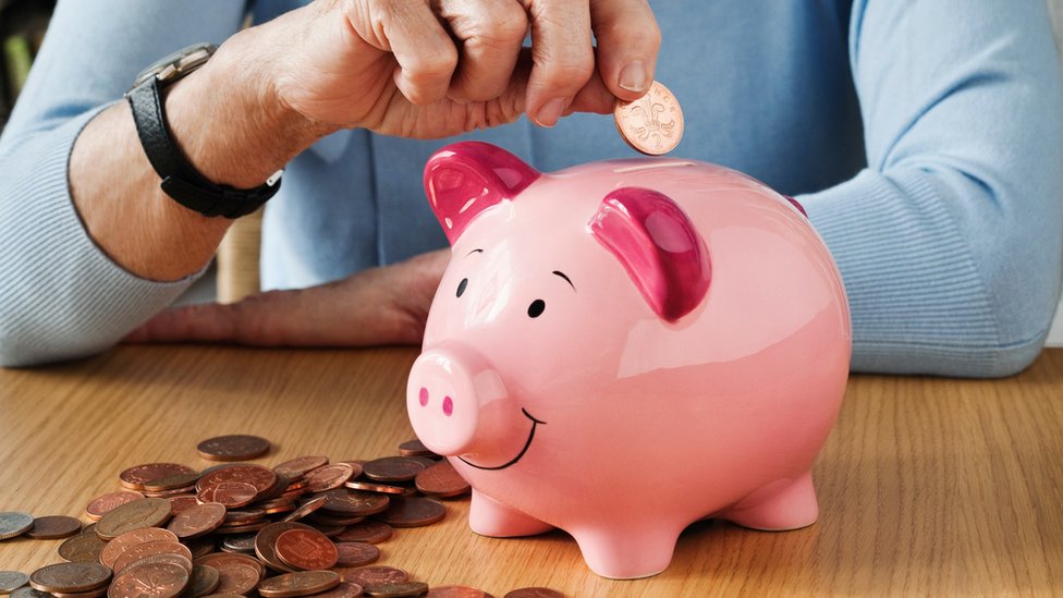 Mãos colocam moedas em um cofre em formato de porquinho