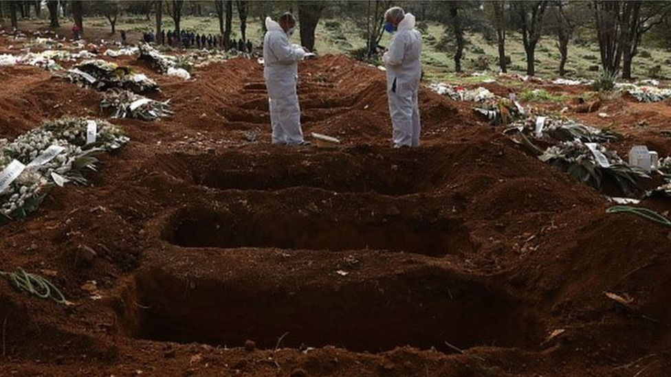 Trabalhadores com equipamentos de proteção cuidam de cova em cemitério