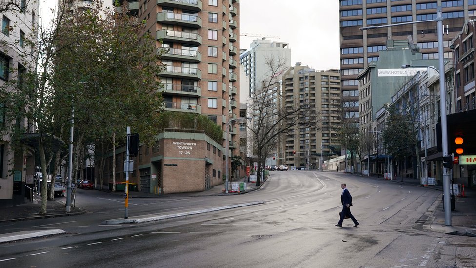 Um homem atravessa uma rua deserta no centro de Sydney durante lockdown