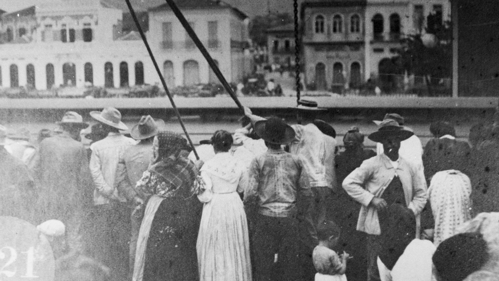 Foto em preto e branco mostra dezenas de homens e mulheres no porto