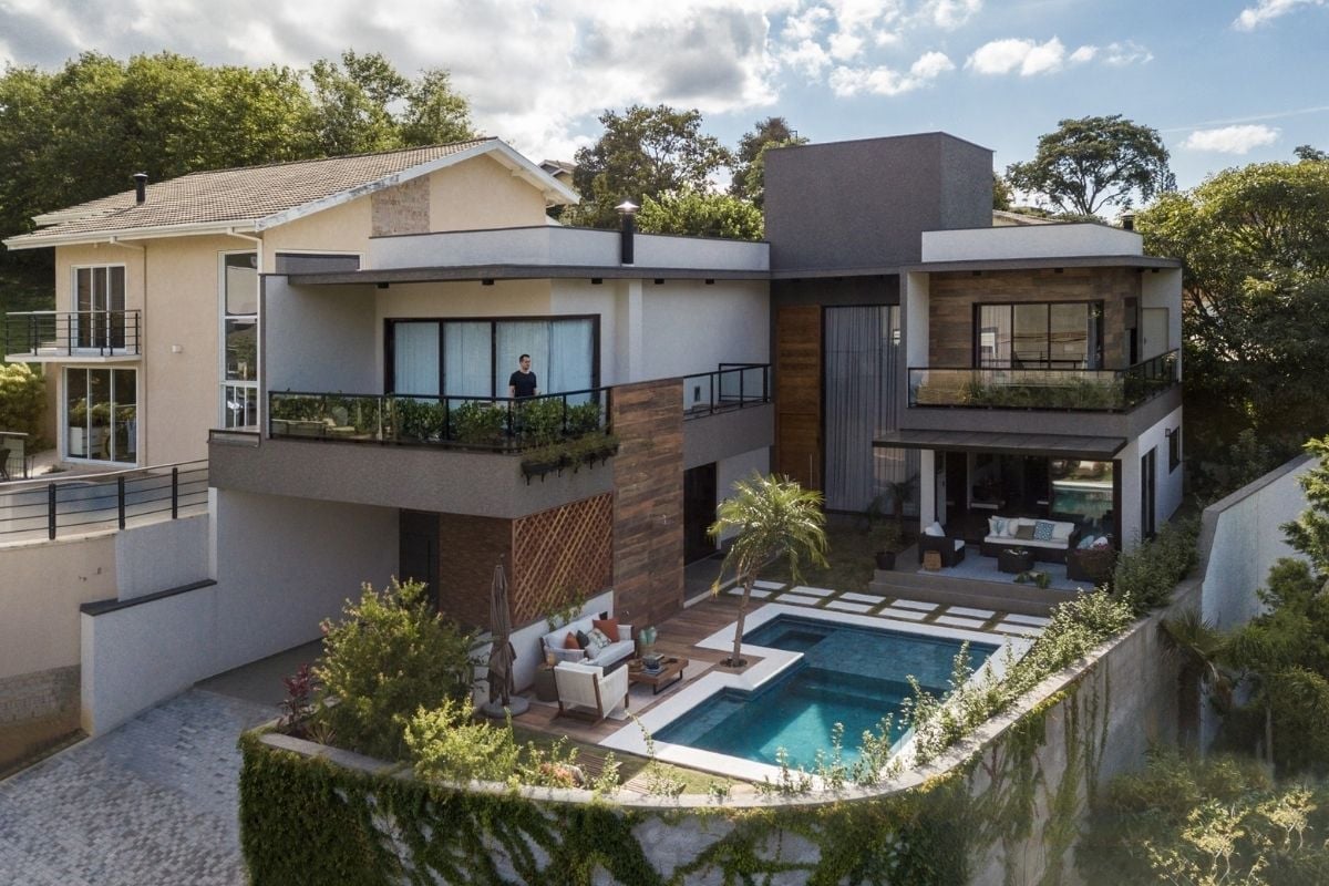 Vista externa de uma casa grande e moderna, cercada de árvores e plantas