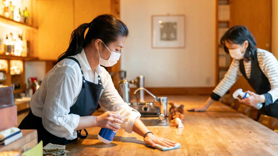 Mulheres de máscara desinfetam mesa