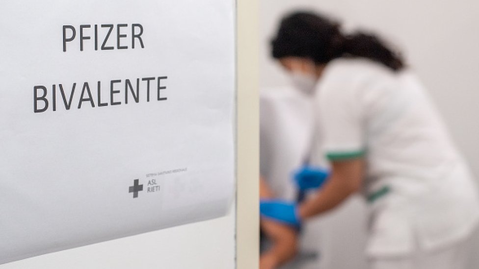 Cartas com os dizeres 'Pfizer bivalente' — ao fundo, profissional de saúde aplica dose de vacina em uma pessoa