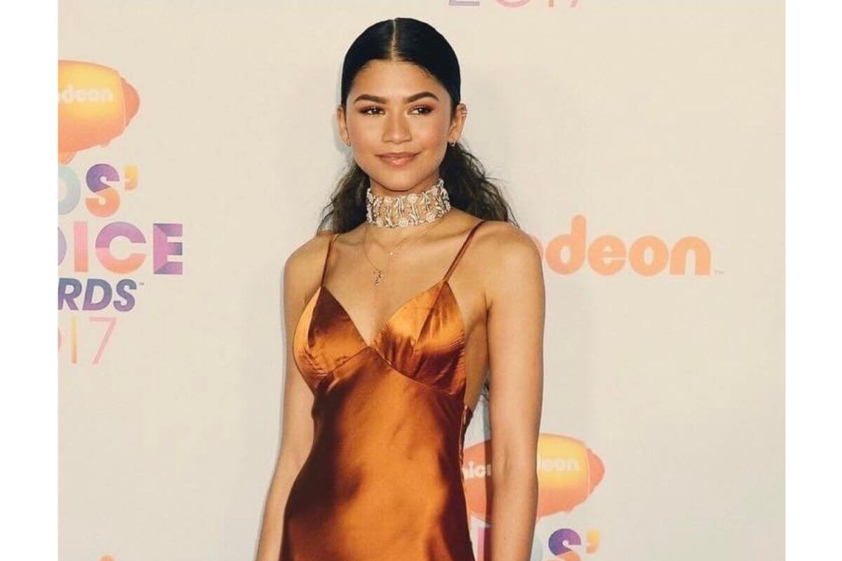 Atriz e cantora Zendaya posando para foto com um vestido laranja 