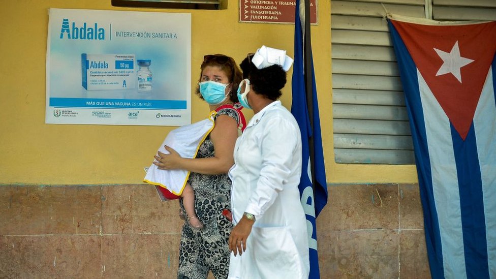 Mulher cubana com bebê ao lado de enfermeira em posto de vacinação em Cuba