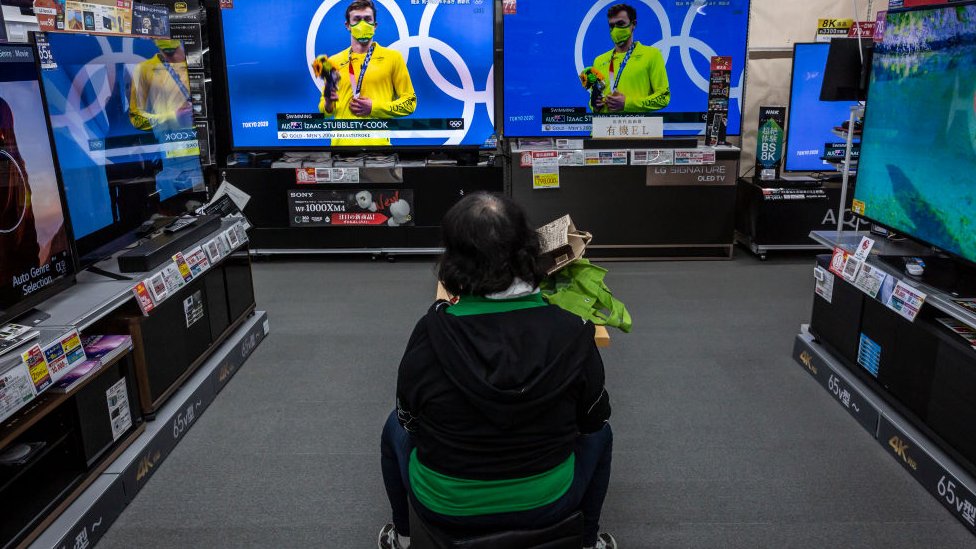 Uma mulher assiste aos jogos das Olimpíadas na televisão em uma loja