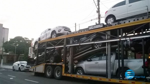 Caminhão cegonha enrosca em fios e derruba carro