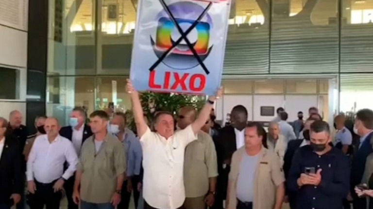 Sem máscara, Bolsonaro causa aglomeração e ergue cartaz com a frase "Globo lixo"