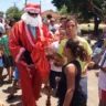 homem vestido com capuz de papai noel entrega sacolas com presentes para grupo de crianças